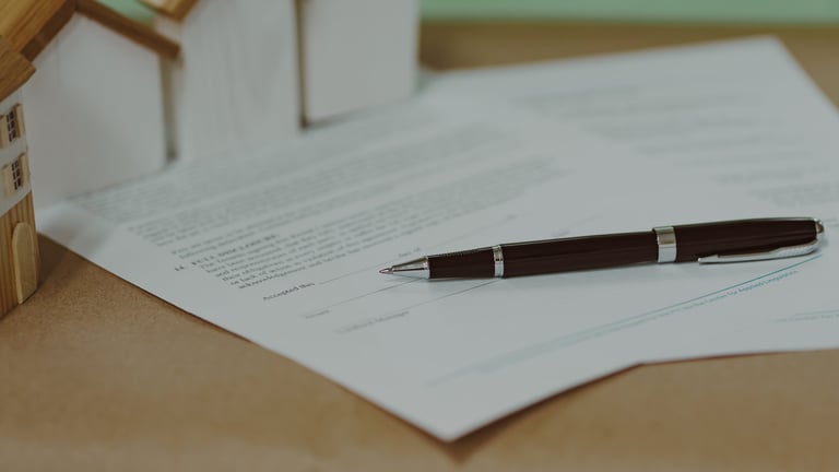 Real estate contract with pen and miniature houses on a desk