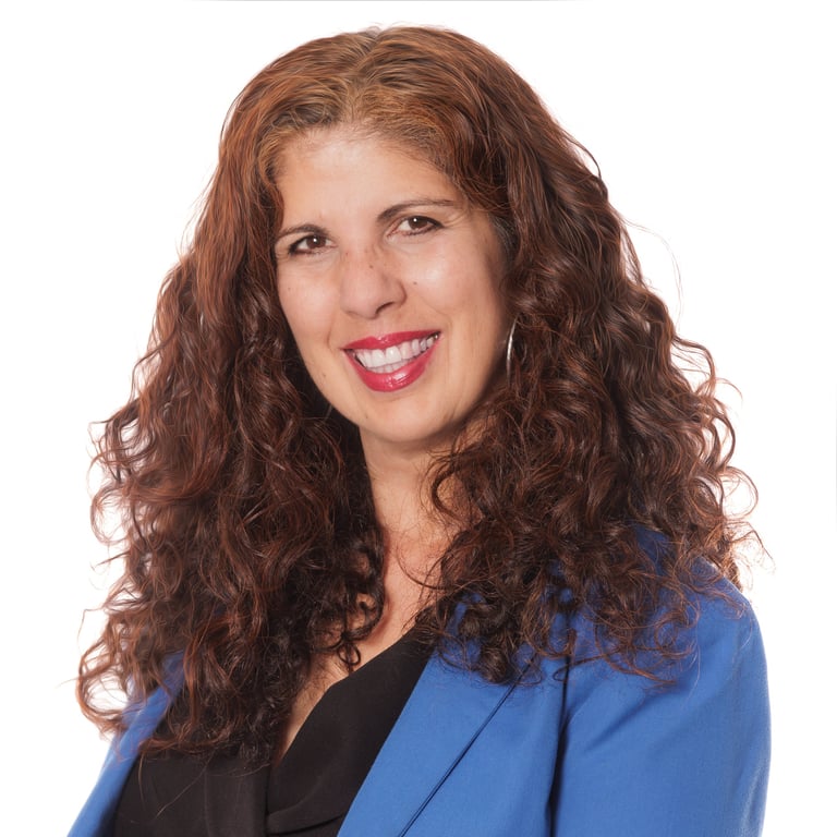 Professional headshot of a woman with long curly reddish-brown hair wearing a blue blazer and black top, smiling against a white background.