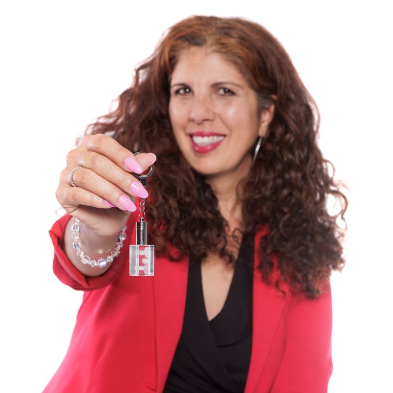 Woman with curly reddish-brown hair wearing a pink blazer, holding a red lipstick bottle and displaying pink manicured nails